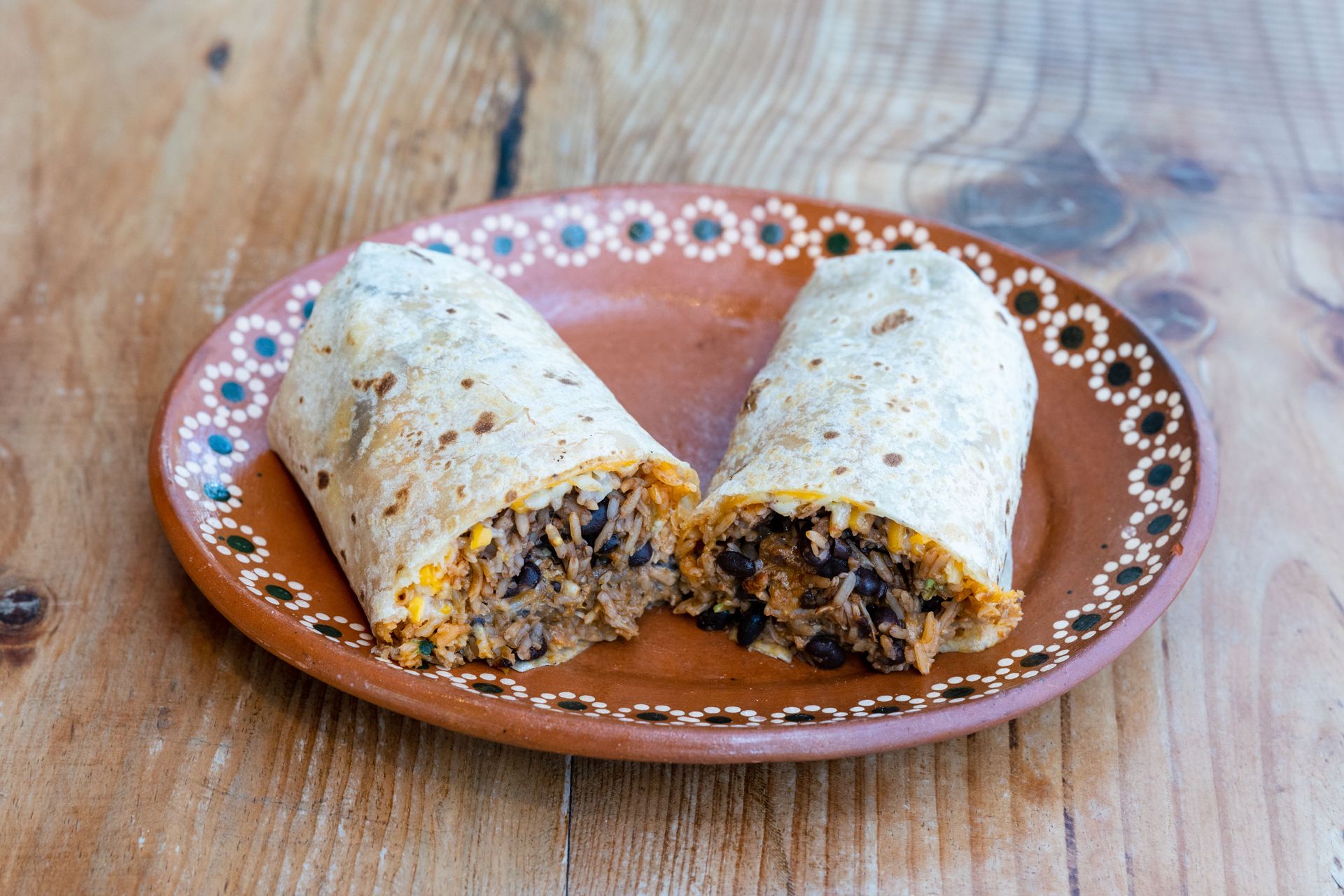 Tasty Mexican burrito split open to show filling on a rustic clay plate.